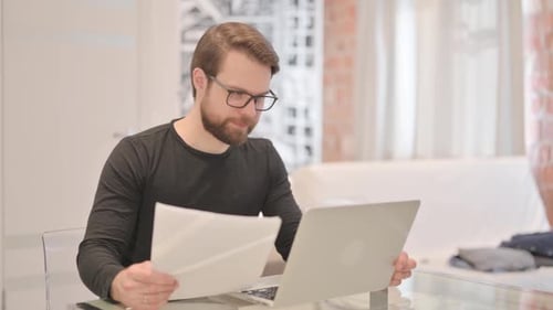 Man Working at Home with Laptop and Paperwork