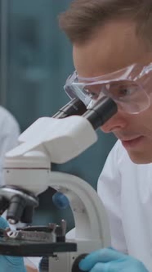 Closeup View of a Scientist Wearing Safety Goggles and Blue Gloves Carefully Using a Microscope in a
