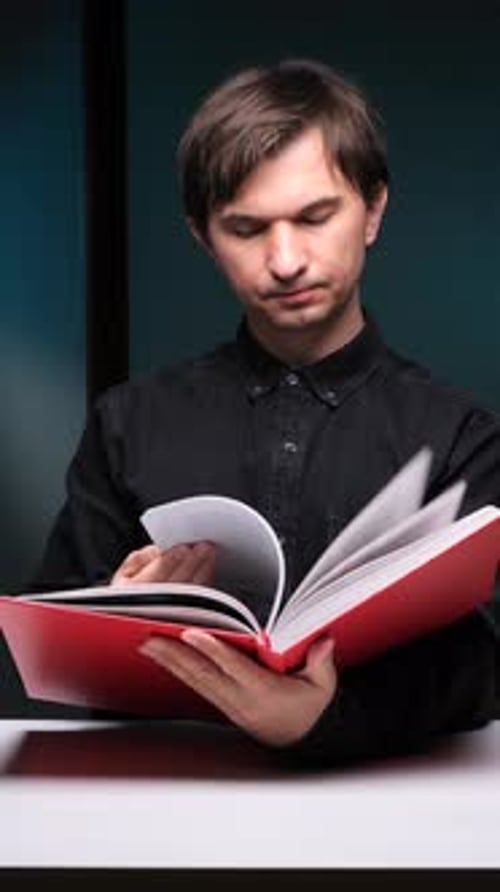 Vertical Video Focused Man Reading a Red Book at Night