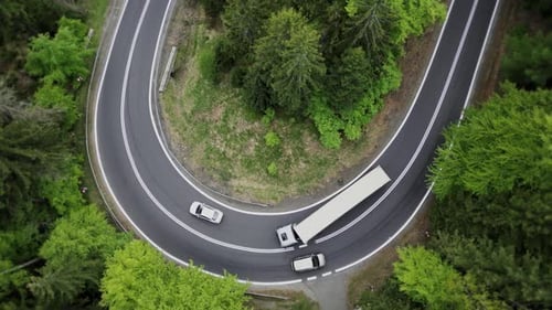 Aerial top view winding asphalt road on a mountain with a moving truck and trailer.