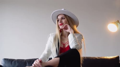 A Woman with Dyed Hair and Makeup in a Hat White Jacket and Red Bra Poses in the Studio