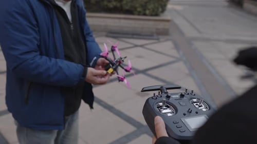 Ein erwachsener Pilot hält einen kleinen FPV-Rennquadcopter und eine Fernbedienung in der Hand, um die Miniaturdrohne vorzubereiten