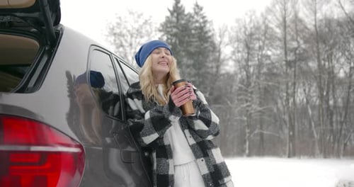 Young Woman with Hot Drink Near Car at Winter Forest