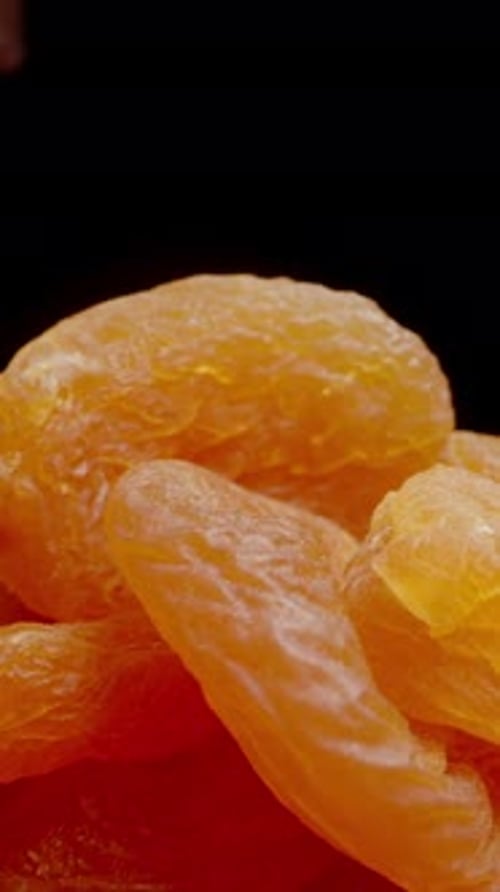 Vertical video. Close-up of a hand picking up a handful of Dried Apricots. Isolated on a black.