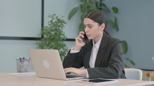 Businesswoman Talking on Phone While Using Laptop