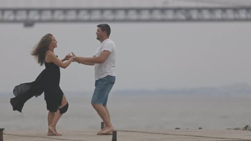 A Cute Romantic Married Couple Dancing on the Pier with a Bridge on the Background
