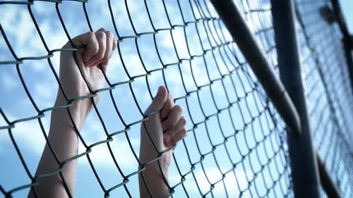 Child's hands on the wire mesh of the refugee camp