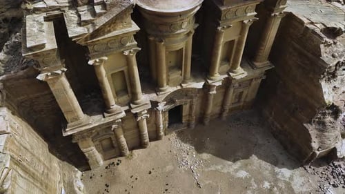 Aerial view away from the Ad Deir monastery, in sunny Petra, Jordan - reverse, tilt, drone shot