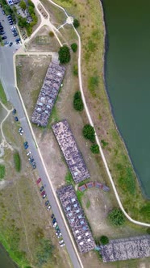 Vista aérea de arriba hacia abajo de antiguos edificios rectangulares cerca de un paseo marítimo. Caminos, árboles y autos estacionados