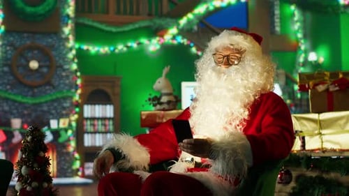 Happy Man Dressed As Santa Claus Looks at Letter Received From Kids on Phone