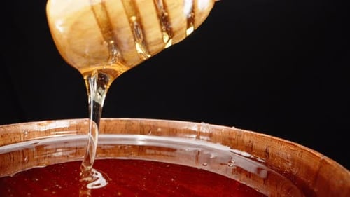 Honey Dripping From Dipper Into Wooden Bowl