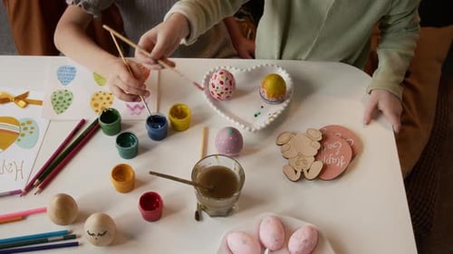 Mains de filles dessinant des motifs sur des œufs de Pâques teints à la maison