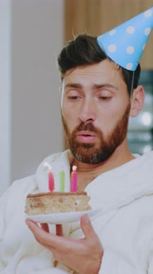 Sad Young Man Celebrates Birthday Alone in the Living Room During Quarantine Blows Out the Candles