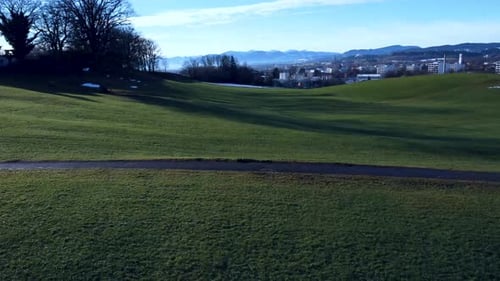 Drone wooshing near to the ground, alps in the distance, flying over a green landscape