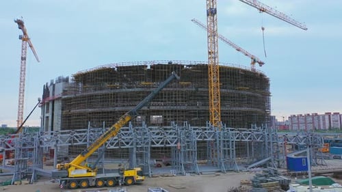 Piezas de estructura de acero y grúa cerca de un estadio deportivo sin terminar