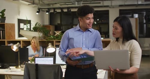 Biracial man and Asian woman discuss business work in an office