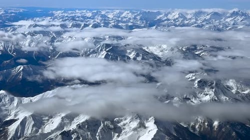 The Snow-covered Alps From the Sky with Some Clouds Covering the Majestic Peaks. Cockpit View.