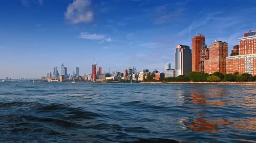 Waves go from a boat traveling by the river. Low angle view at the skyline of New York