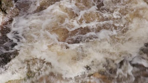 Wildes Bachwasser fließt über untergetauchte Felsen und erzeugt wirbelnde, schaumige Texturen.