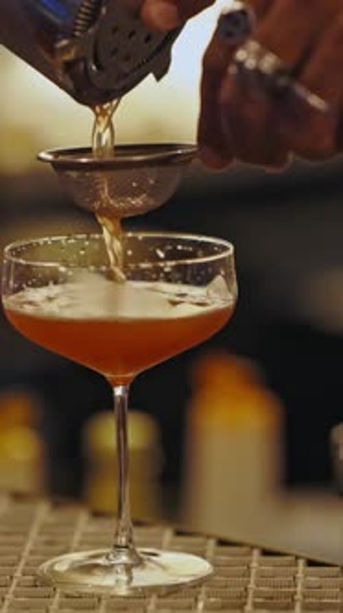 Bartender Pouring Cocktail Through Strainer into Glass