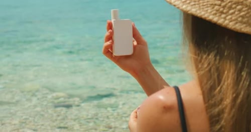 Woman holding sunscreen bottle by the clear turquoise sea on a sunny summer day
