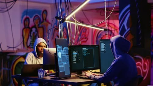 Hooded Hackers Typing Code at Computers at Night