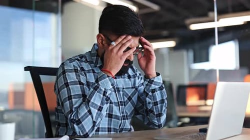 Man at Desk with Headache in Modern Office