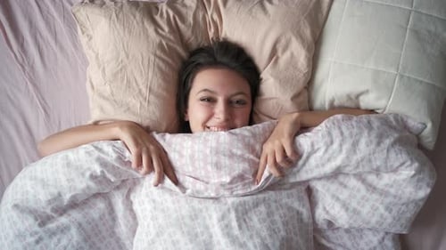 Smiling Woman Lying in Bed Under Duvet