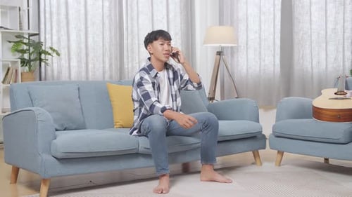 Young Man Talking on Smartphone on Couch at Home