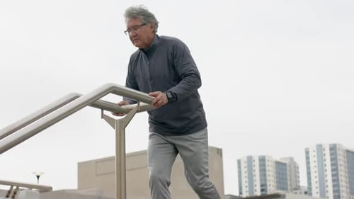 Homem sênior se aproximando do corrimão da escada, subindo e estendendo os braços para se aquecer no terraço