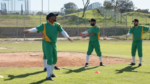 Training cone initiating diverse baseball players rotating arms forward and back warming on infield
