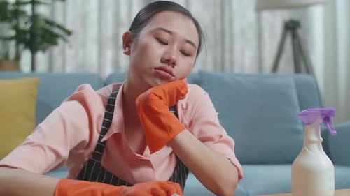 Nahaufnahme einer traurigen asiatischen Haushälterin mit einer Schürze, die den Tisch am Spray zu Hause putzt