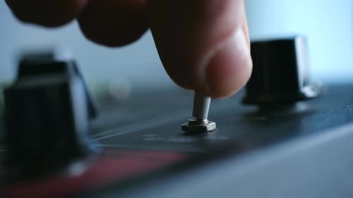 Vista detallada de la activación de un pequeño interruptor en el panel de sintetizador clásico iluminado por Studio Lighting