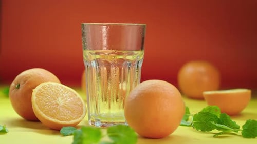Dropping ice blocks in an empty highball glass, surrounded by fresh oranges and spearmint, isolated