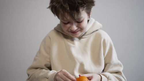 Smiling Caucasian kid peeling the tangerine. Healthy lifestyle, child consuming fruit at home.
