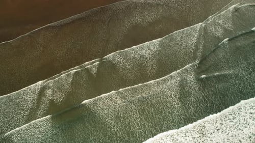 Top view of rhythmic ocean waves rolling slowly over sandy tropical shoreline