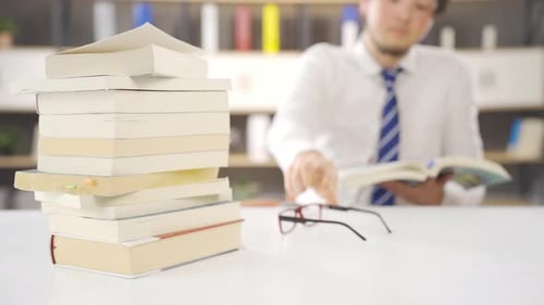 Mann liest ein Buch zwischen einem Stapel Bücher.