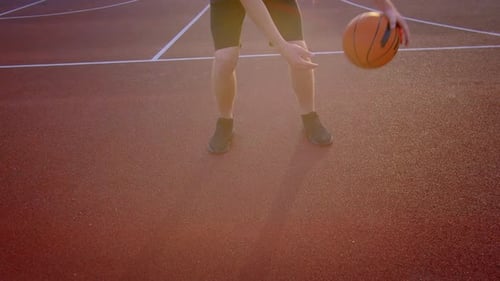 An Athlete Practices with a Basketball on a Sports Court in the Setting Sun