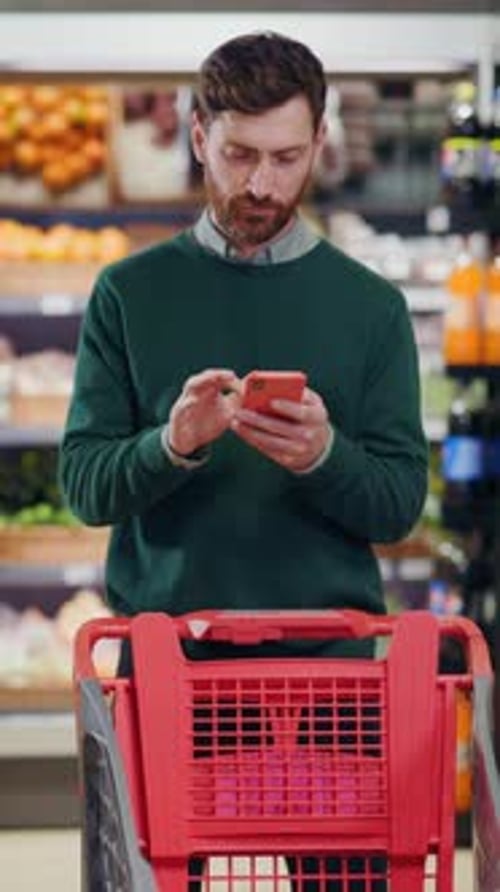 A Man is Shopping with His Smartphone While He is in a Grocery Store Looking for Items