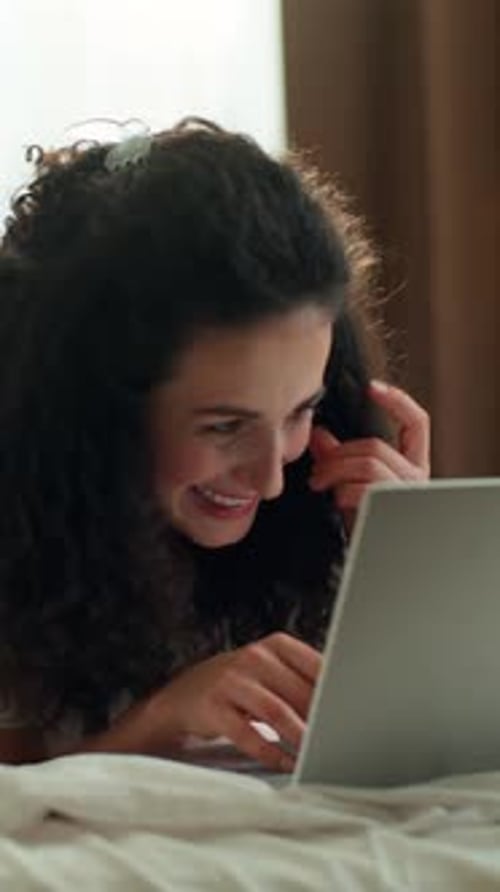 Femme caucasienne détendue utilisant un ordinateur portable discutant en ligne sur les réseaux sociaux allongée dans son lit le matin en souriant