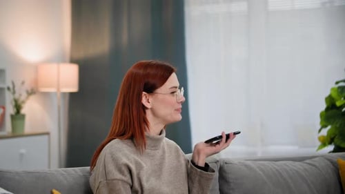 Fröhliche Frau mit Brille spricht mit einem Freund auf dem Handy auf dem Smartphone, während sie sich zu Hause entspannt
