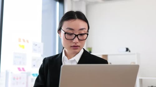 Confident Asian Businesswoman Holding Laptop in Modern Office Setting