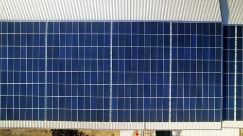 Aerial drone view of multiple solar panels on the roof of a manufacturing building. Ecology thematic
