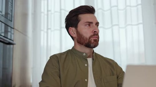 Pensive Bearded Guy with Laptop Looking Aside During Working Day at Home Office