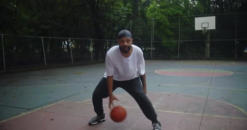 Homme d'ascendance africaine dribble au basket entre les jambes sur un terrain extérieur, faisant preuve de concentration, d'habileté et