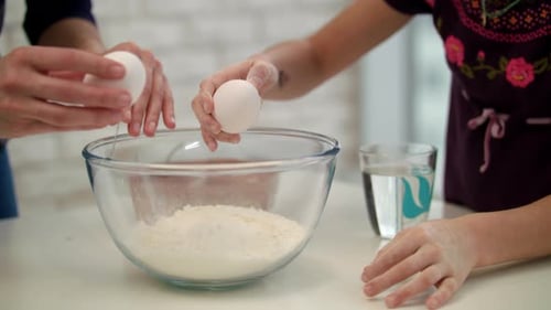 Child Cracking Eggs into Bowl with Adult Helper