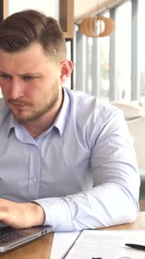 Frustrated Businessman Grapples with Laptop Fatigue in a Modern Cafe