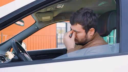 Un jeune homme se frotte les yeux avec lassitude en conduisant une voiture
