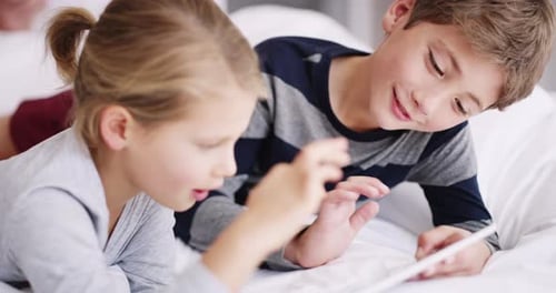 Siblings Using Tablet Together on Bed
