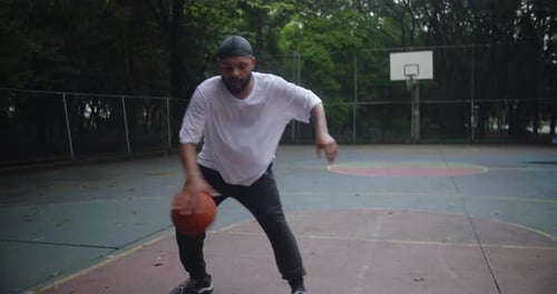 Homme d'ascendance africaine dribble au basket entre les jambes sur un terrain urbain extérieur, montrant son contrôle,